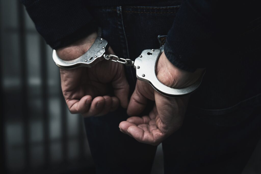 arrested man with cuffed hands behind prison bars - Can You Get Bond for A Felony? - Air Capital Bail Bonds in Wichita, Kansas