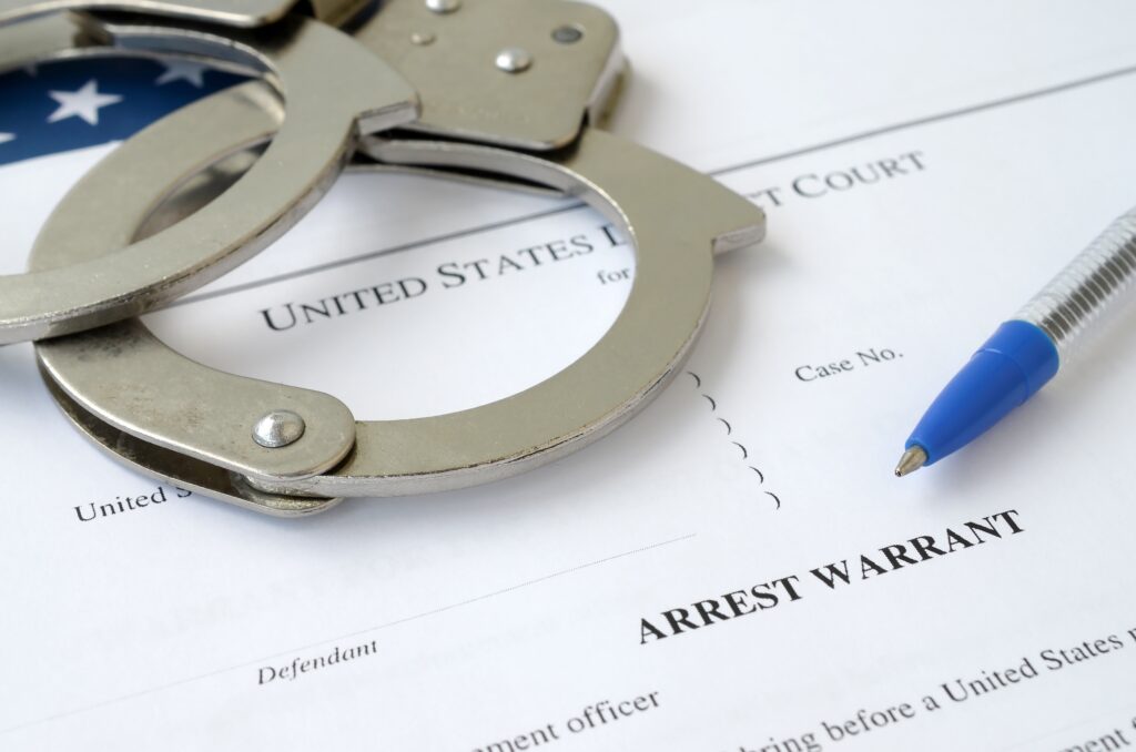 District Court Arrest Warrant court papers with handcuffs and blue pen on United States flag. Concept of permission to arrest suspect - How To Turn Yourself In for A Warrant - Air Capital Bail Bonds in Wichita, Kansas